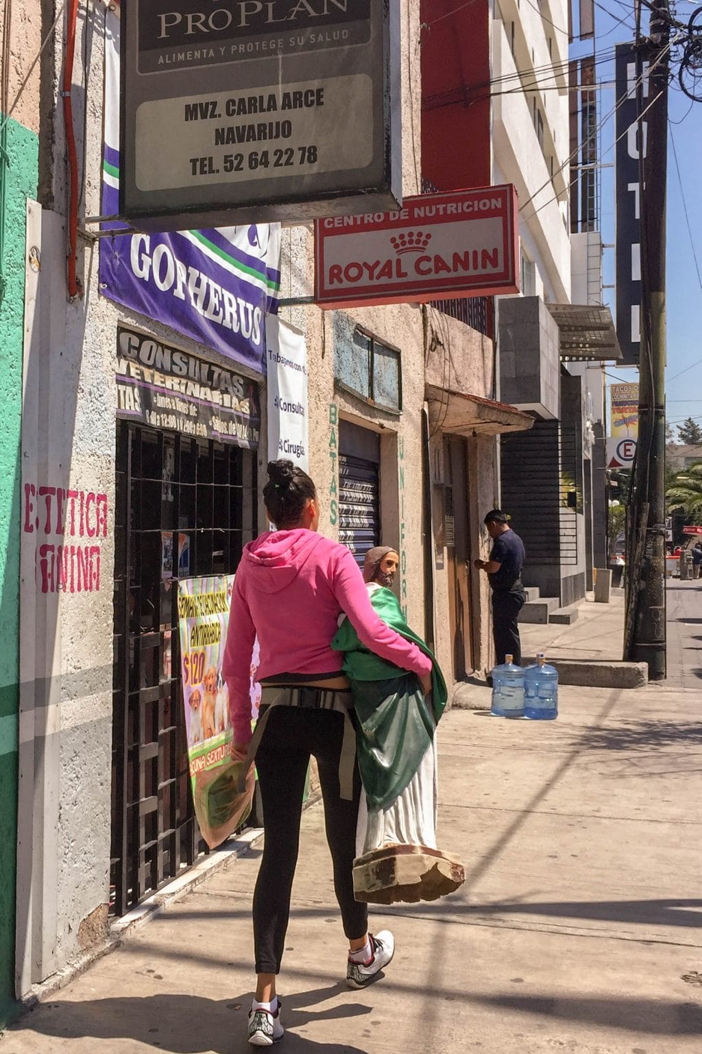 street scene of woman in pink shirt carrying a large statue of St Jude in CDMX.